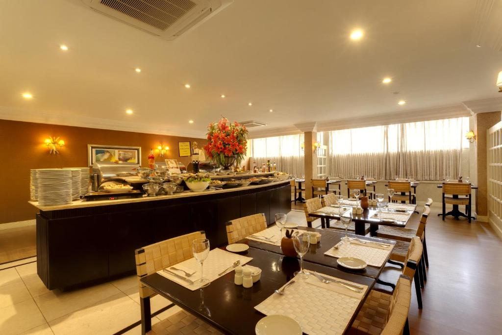 Sala de jantar de restaurante iluminada com mesas postas, longo balcão de buffet escuro e iluminação quente no teto.