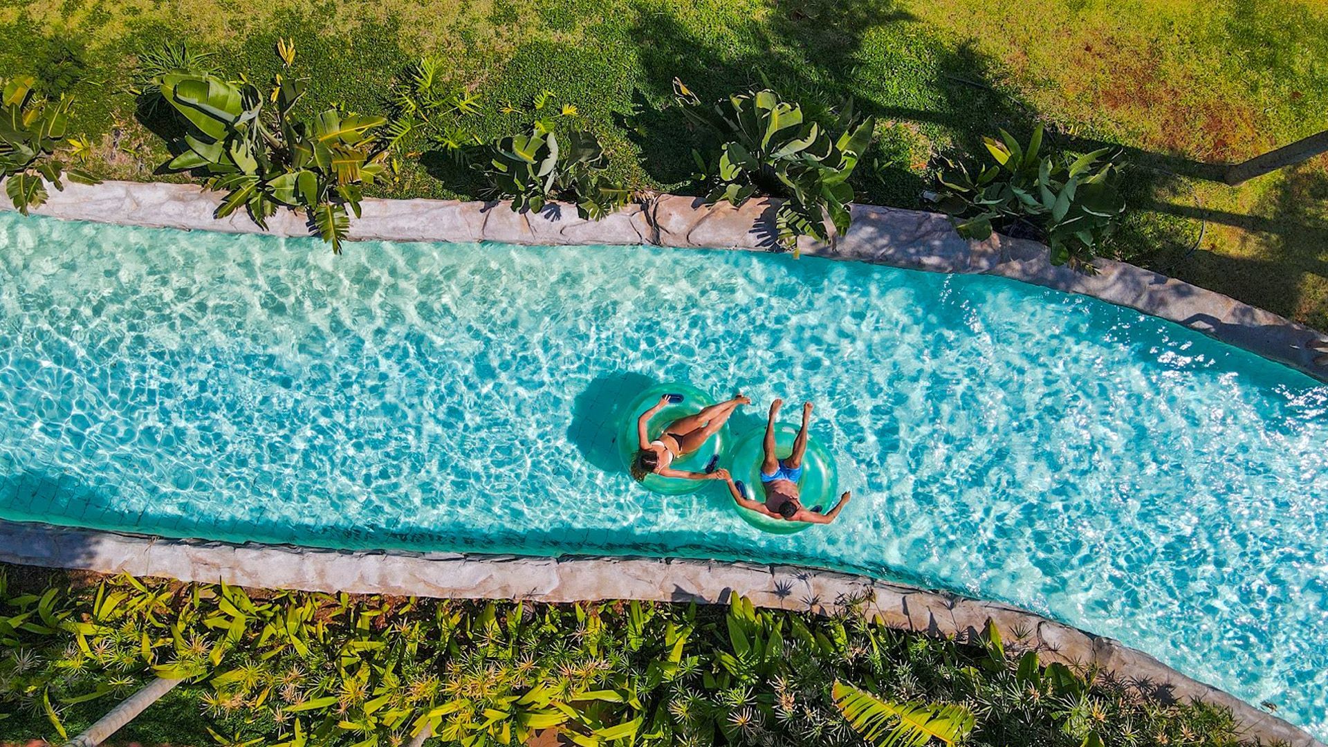 Uma pessoa flutua em uma piscina turquesa, cercada por vegetação tropical.