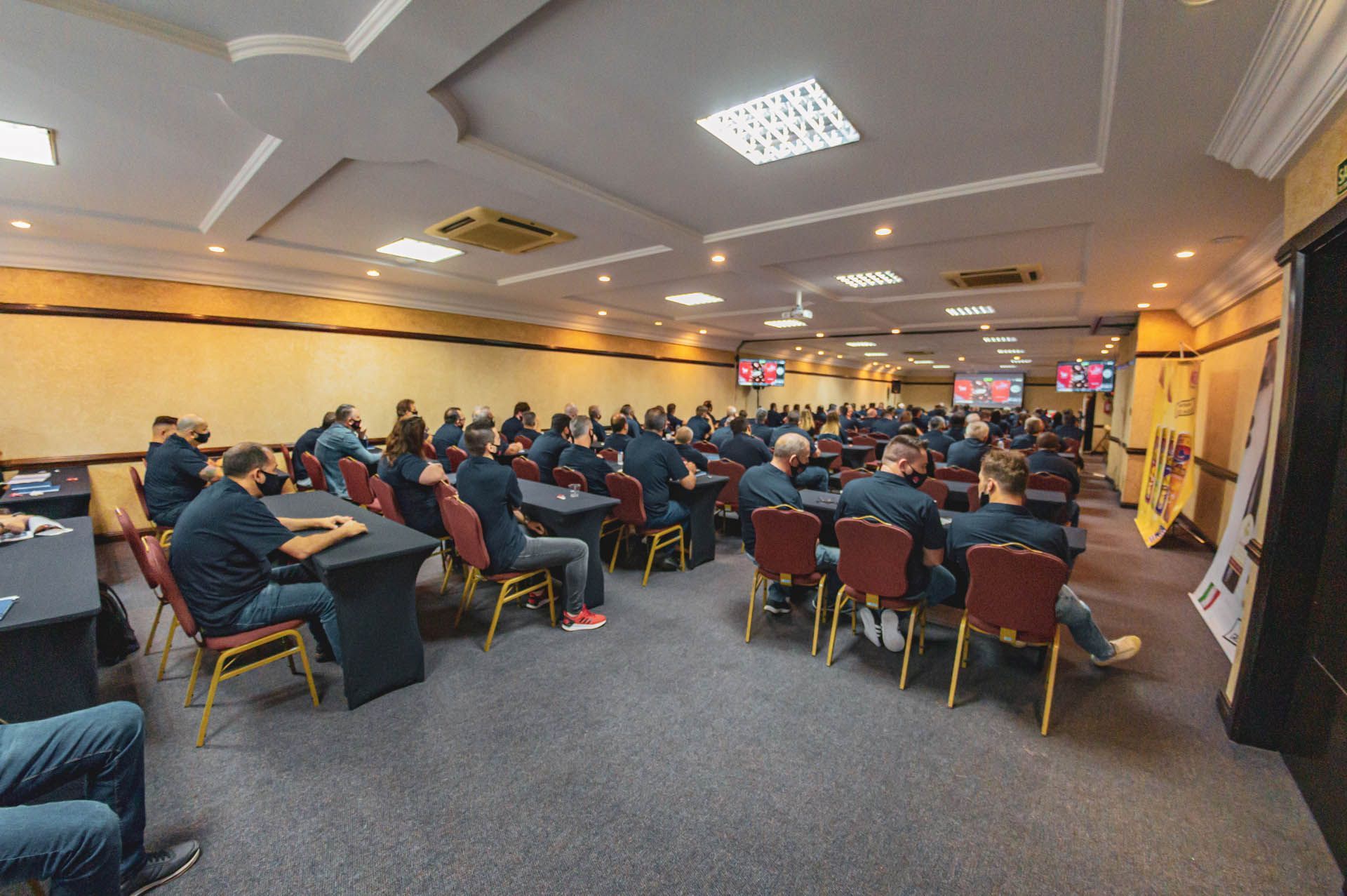 Pessoas sentadas em uma sala de conferências assistindo a uma apresentação em telões.