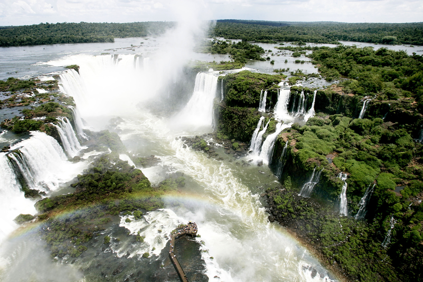 Ampla cascata de cachoeira em meio a uma exuberante floresta verde, com névoa subindo sobre vários penhascos.