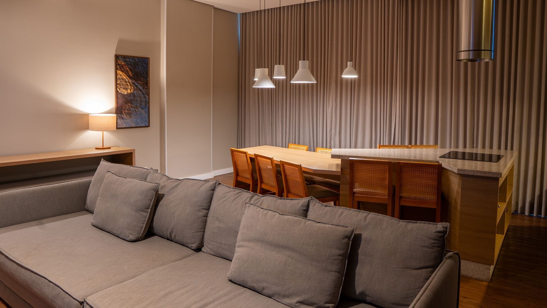 Sala de estar moderna com sofá cinza, mesa de jantar de madeira, luminárias pendentes e parede listrada como destaque.