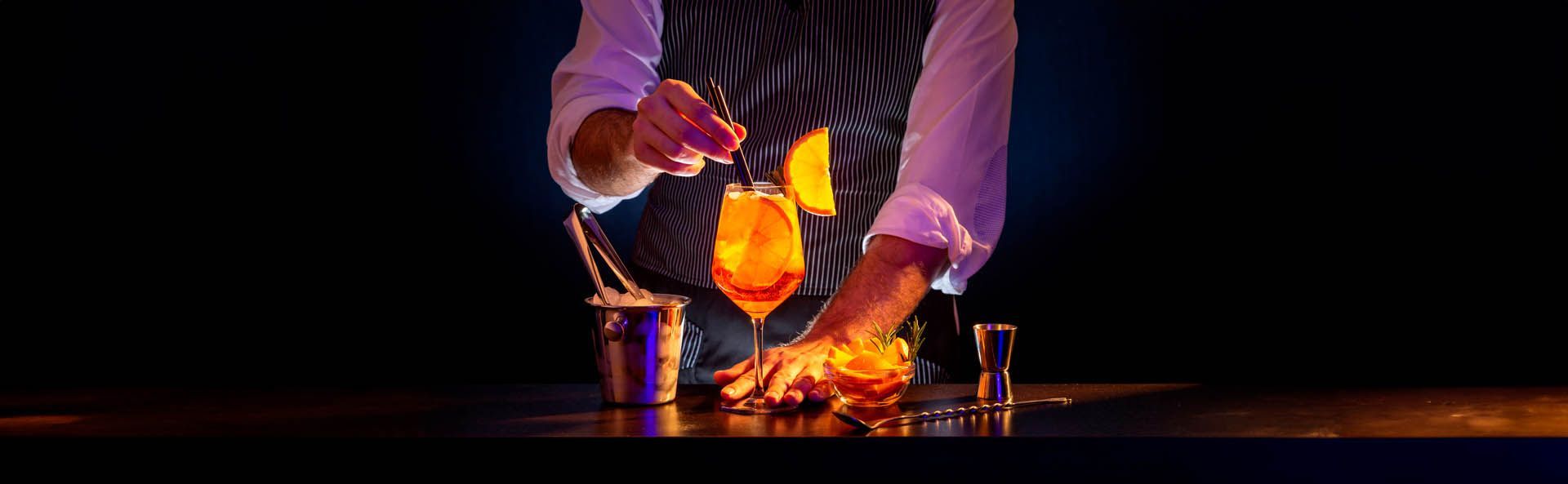 Chef despeja líquido em chamas em um copo sobre um balcão escuro de bar.
