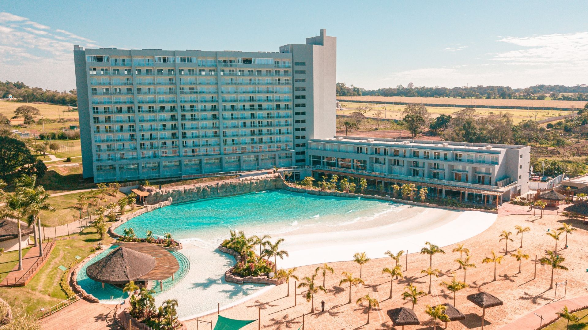 Ampla piscina turquesa de resort ao lado de um hotel moderno em uma paisagem desértica ensolarada.
