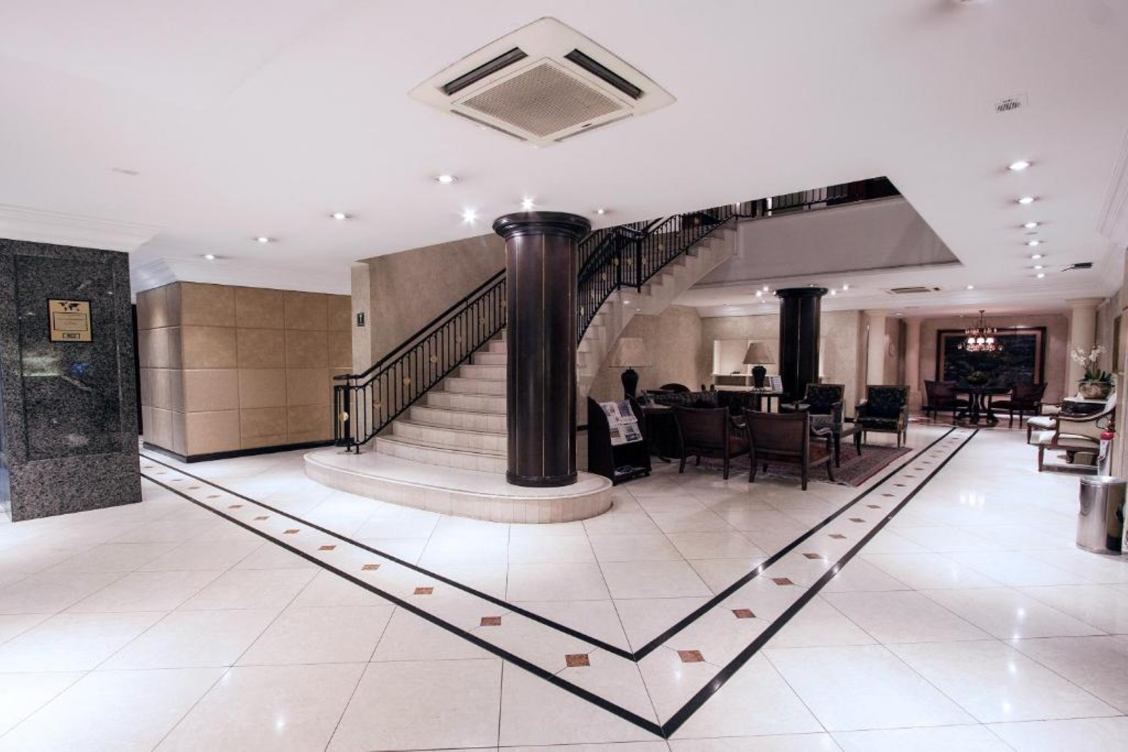 Lobby de hotel de luxo com escadaria curva, piso de azulejos brancos brilhantes e área de estar.