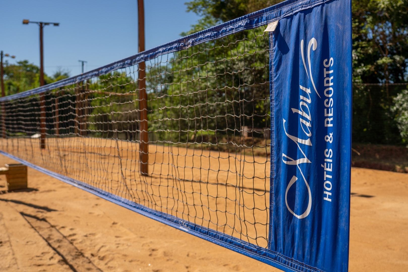 Rede de vôlei azul em uma quadra de areia, com a marca do hotel e resort no poste.