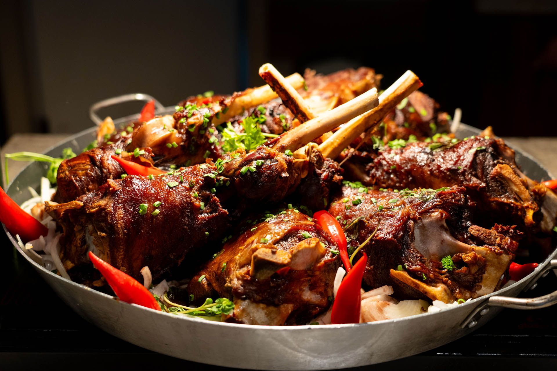 Prato com espetinhos de carne grelhada, decorados com ervas e pimentões vermelhos, sobre uma mesa escura.