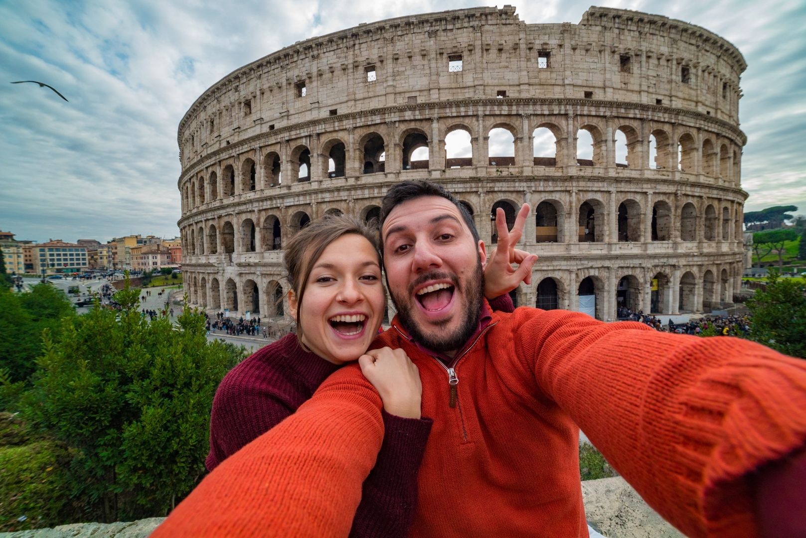 Selfie de duas pessoas sorridentes com suéteres vermelhos em frente ao Coliseu em Roma.