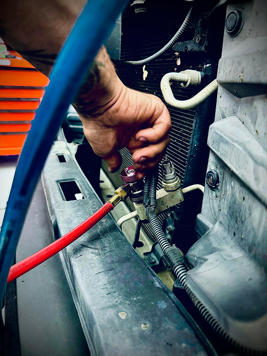A mechanic connects hoses to a car's AC system. Red and blue hoses, close-up on a vehicle's radiator. | King's Auto LLC