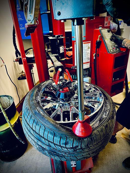 Tire being removed from a chrome wheel on a red tire machine in a shop. | King's Auto LLC