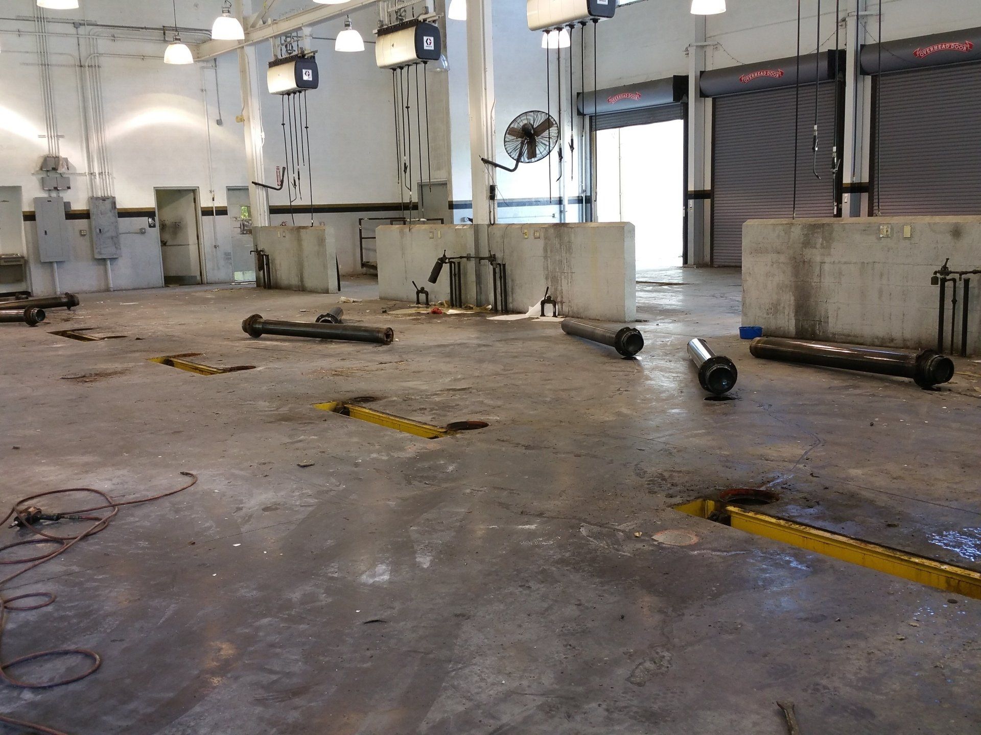 Empty commercial auto repair bay with concrete floor, industrial lighting, and detached metal lift components.
