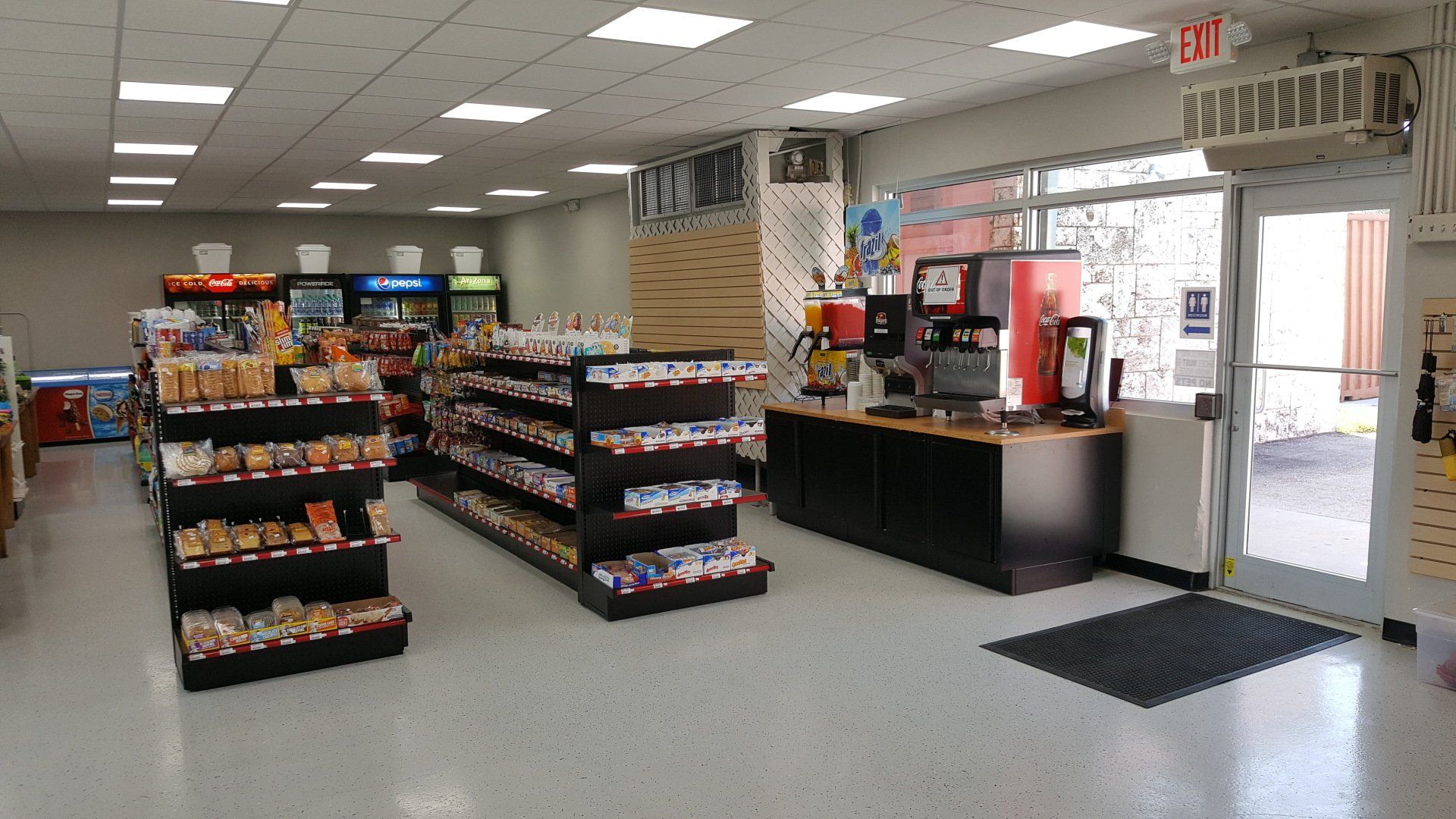 Interior of a clean, well-lit convenience store featuring aisle shelves stocked with snacks and a beverage station.