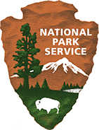 The National Park Service arrowhead emblem, featuring a tree, a mountain range, and a bison against a rust and green field.