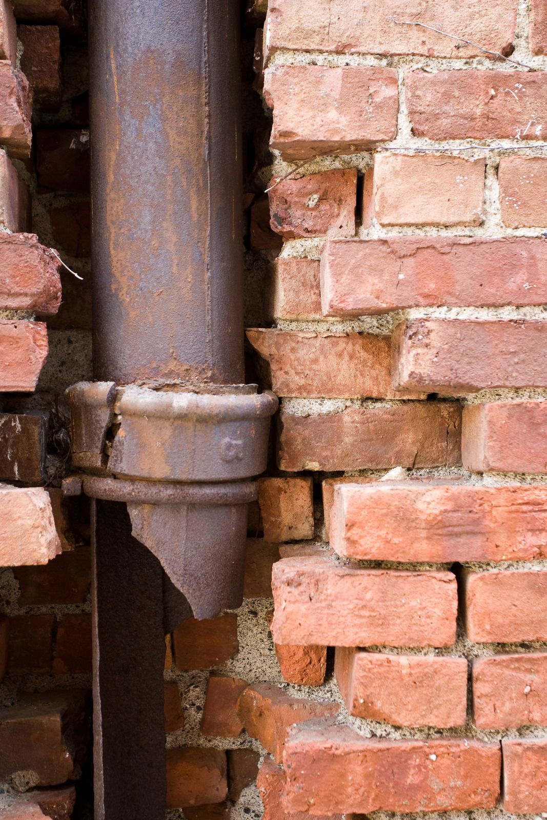 A rusty pipe is attached to a brick wall.