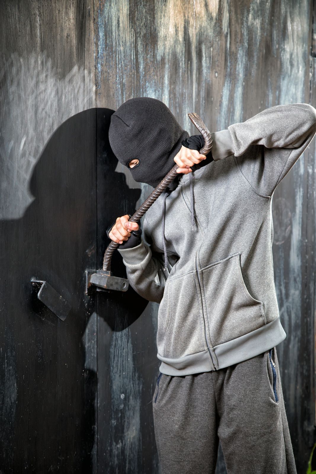 A man in a mask is holding a crowbar in front of a wall.