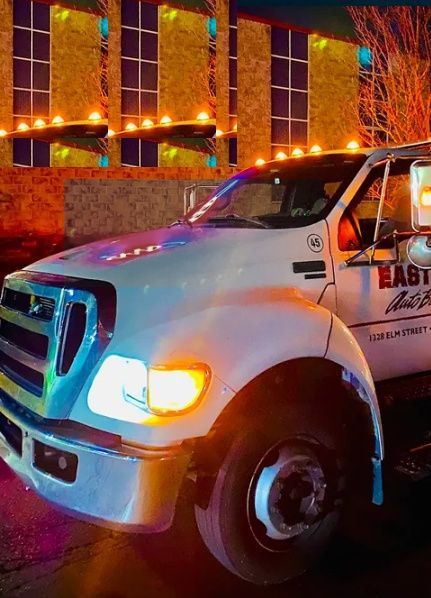 Tow truck parked in front of AAA building, neon sign lit. | Easton Auto Body