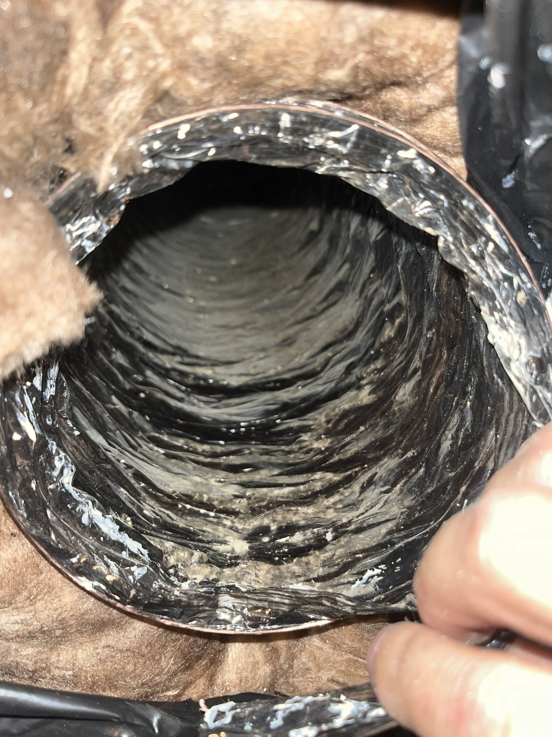 Close-up of a black corrugated pipe interior with white residue, held open by a hand