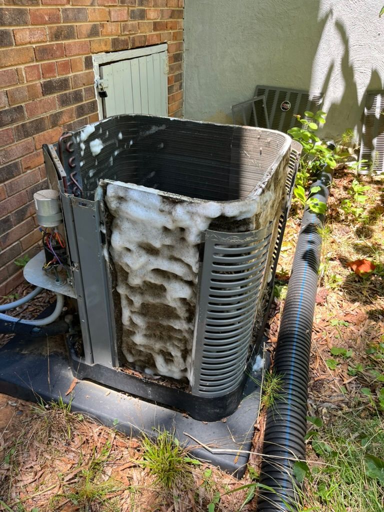 Outdoor HVAC unit with frost and snow buildup beside a brick house and garden hose