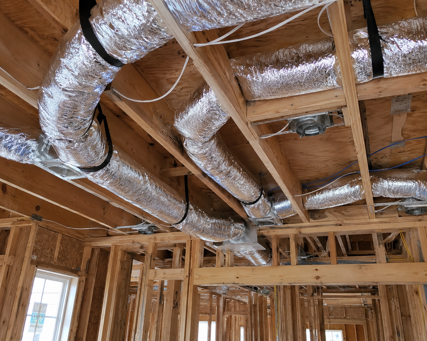Exposed HVAC ducts and wooden framing in an unfinished house interior.