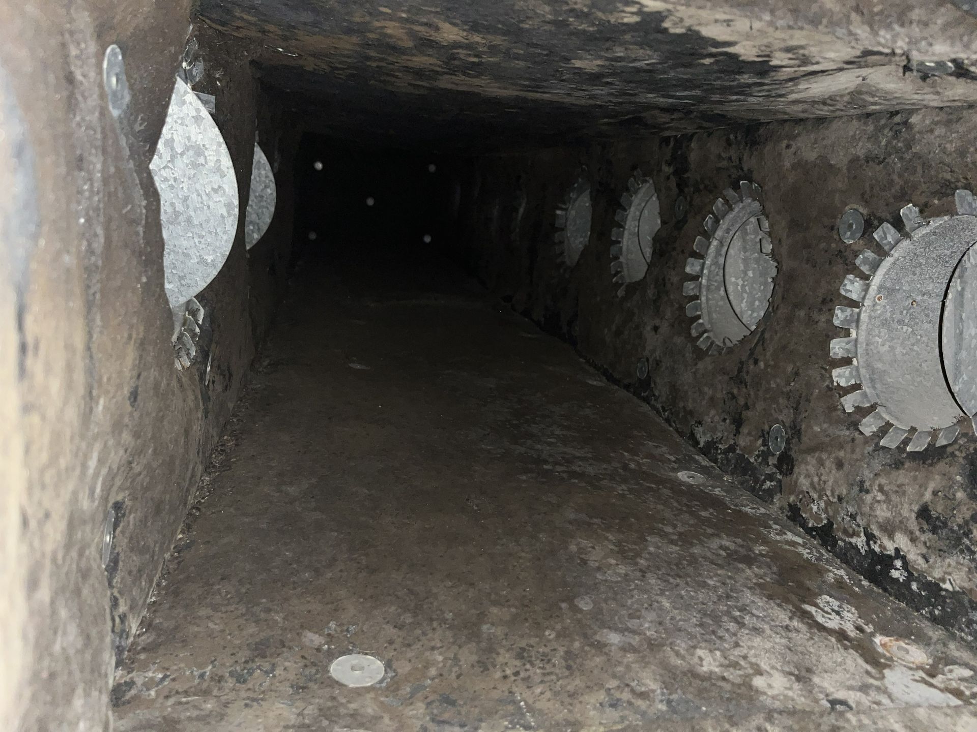 Dark concrete tunnel with circular openings along both walls, viewed from one end.