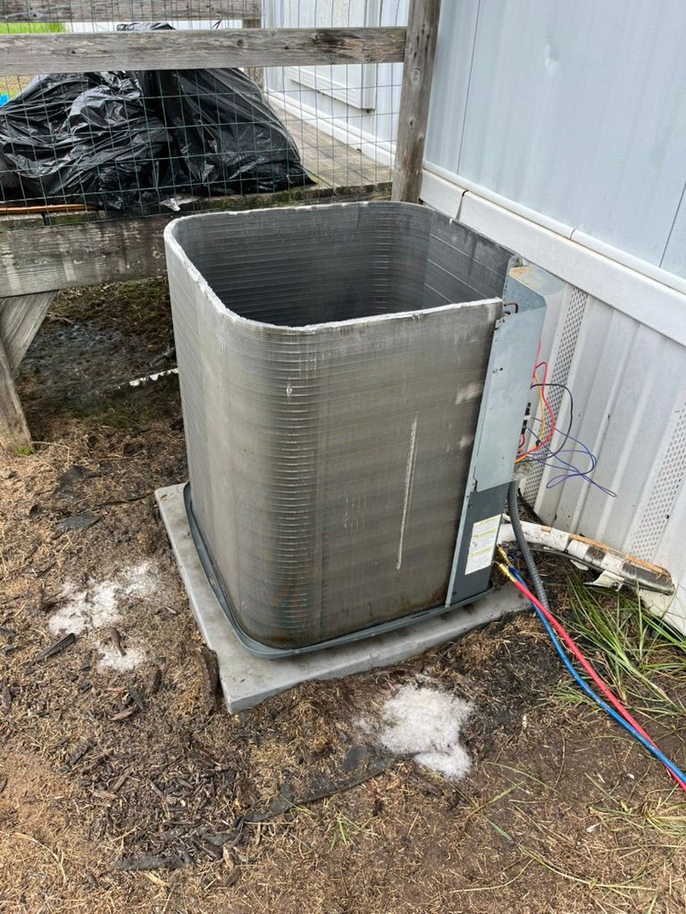Outdoor HVAC unit beside a metal-sided building, with a tarp-covered object and colored hoses nearby