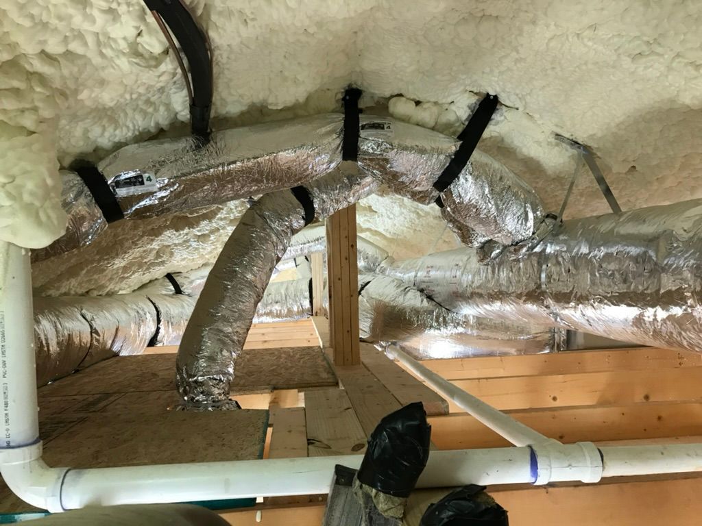 Attic with spray foam insulation, reflective ducting, and exposed pipes and beams
