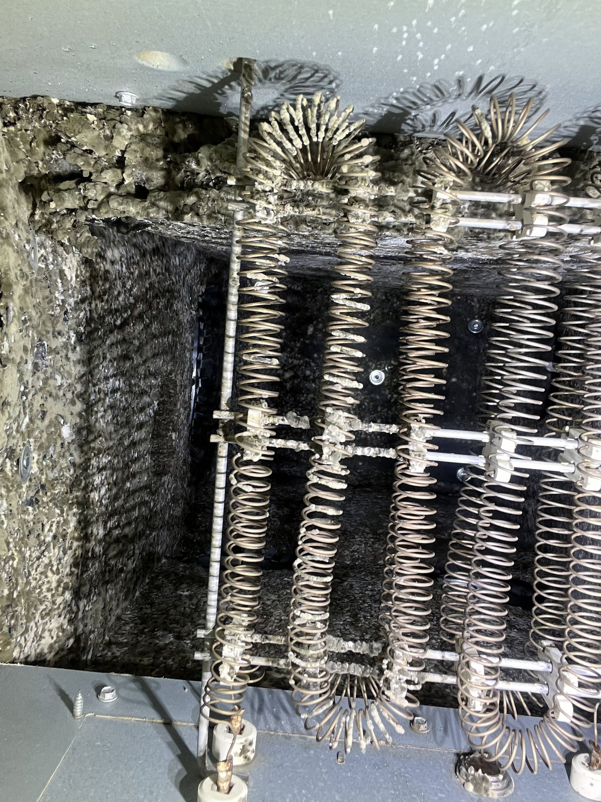 Close-up of a dusty metal coil heating element with charred insulation and debris on the left