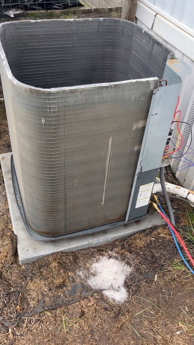 Outdoor gray HVAC unit beside a house, with frost on the ground and colorful hoses nearby.