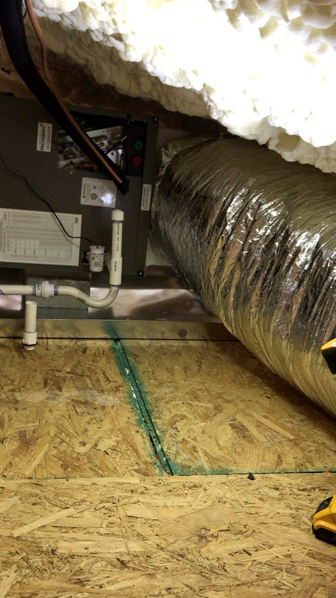 Insulated duct and HVAC equipment in a crawlspace with exposed wood flooring and foam insulation.