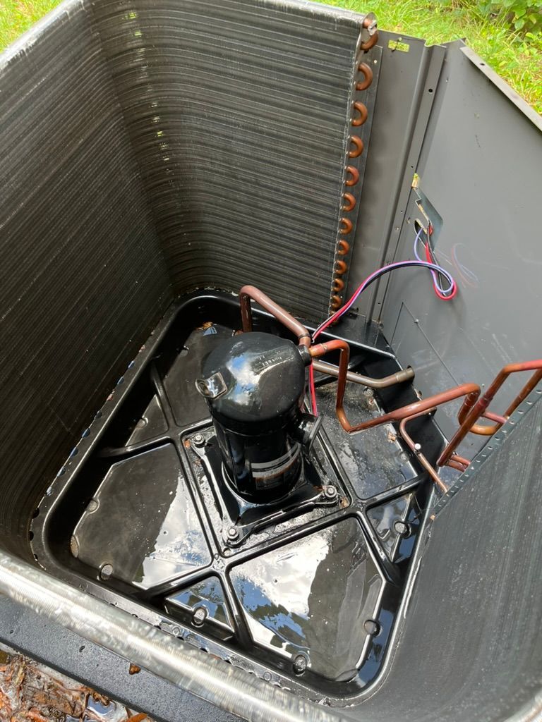Inside an HVAC unit, a black compressor with copper tubing and wiring in a metal housing.