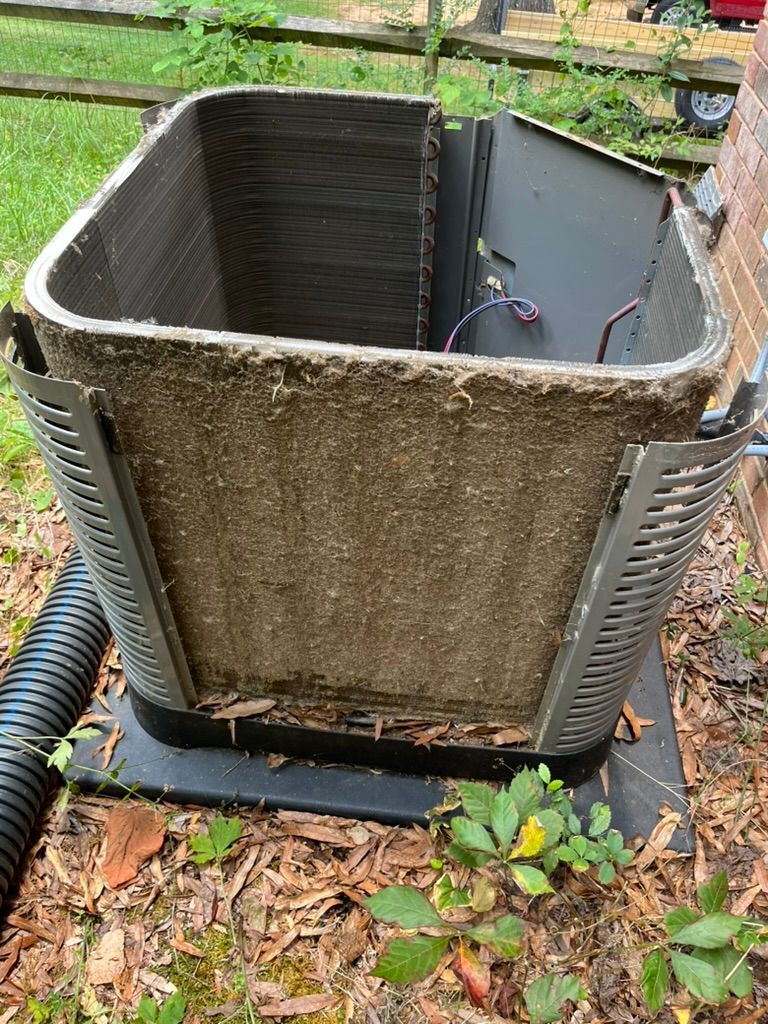 Open HVAC unit with a green, mossy exterior and exposed interior wiring on a concrete pad outdoors.