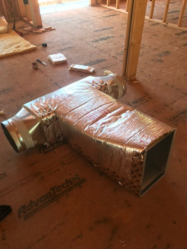 Damaged silver ductwork lying on a dusty unfinished floor in a construction space