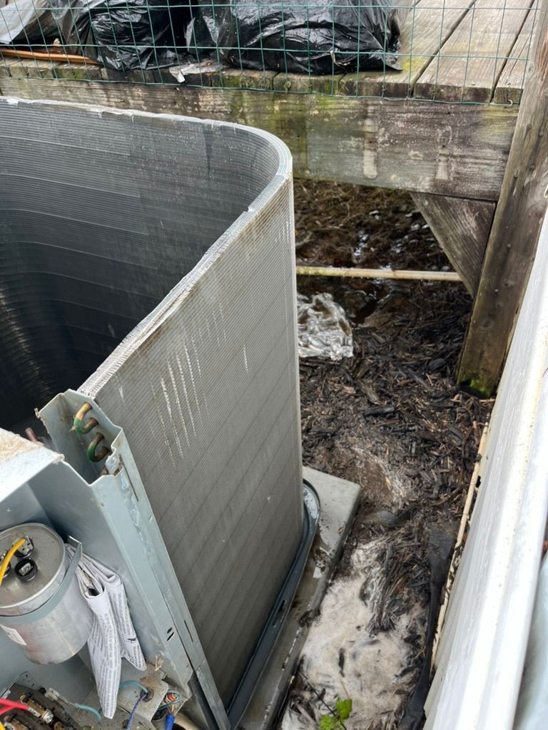 Outdoor HVAC unit beside a building, with muddy ground and debris near a concrete wall