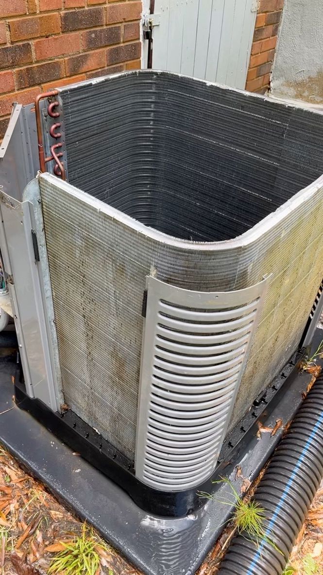 Outdoor HVAC condenser unit beside a brick wall, with a bent silver coil and black top cover