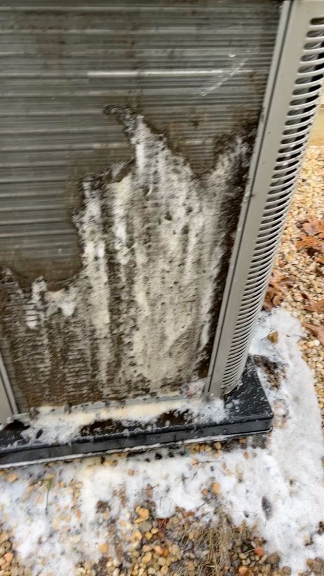 Icy, snow-covered metal outdoor air conditioner unit with frost buildup on the front grille.