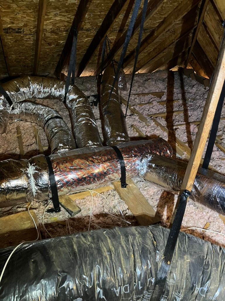 Insulated HVAC ducts in an attic with exposed rafters and foil-wrapped pipes.