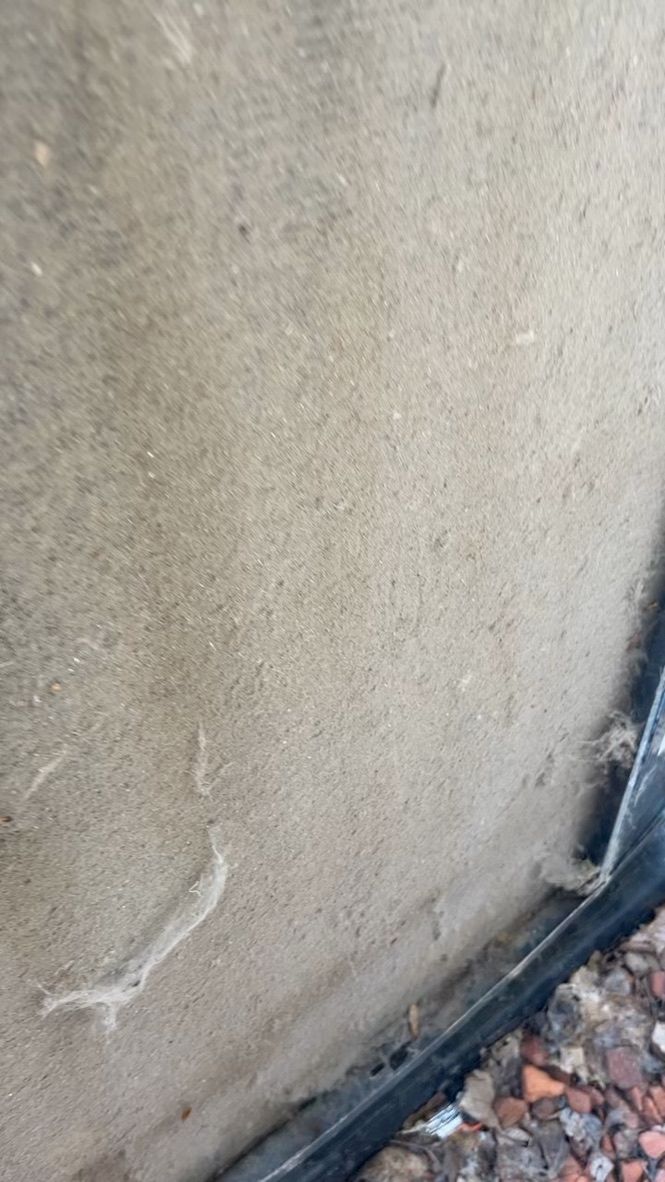 Close-up of a beige concrete wall with a small crack near the bottom and gravel along the edge