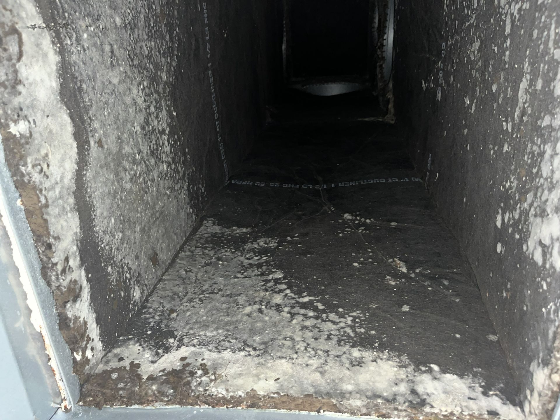 Dark, narrow concrete vent or duct interior with rough, dirty walls and floor