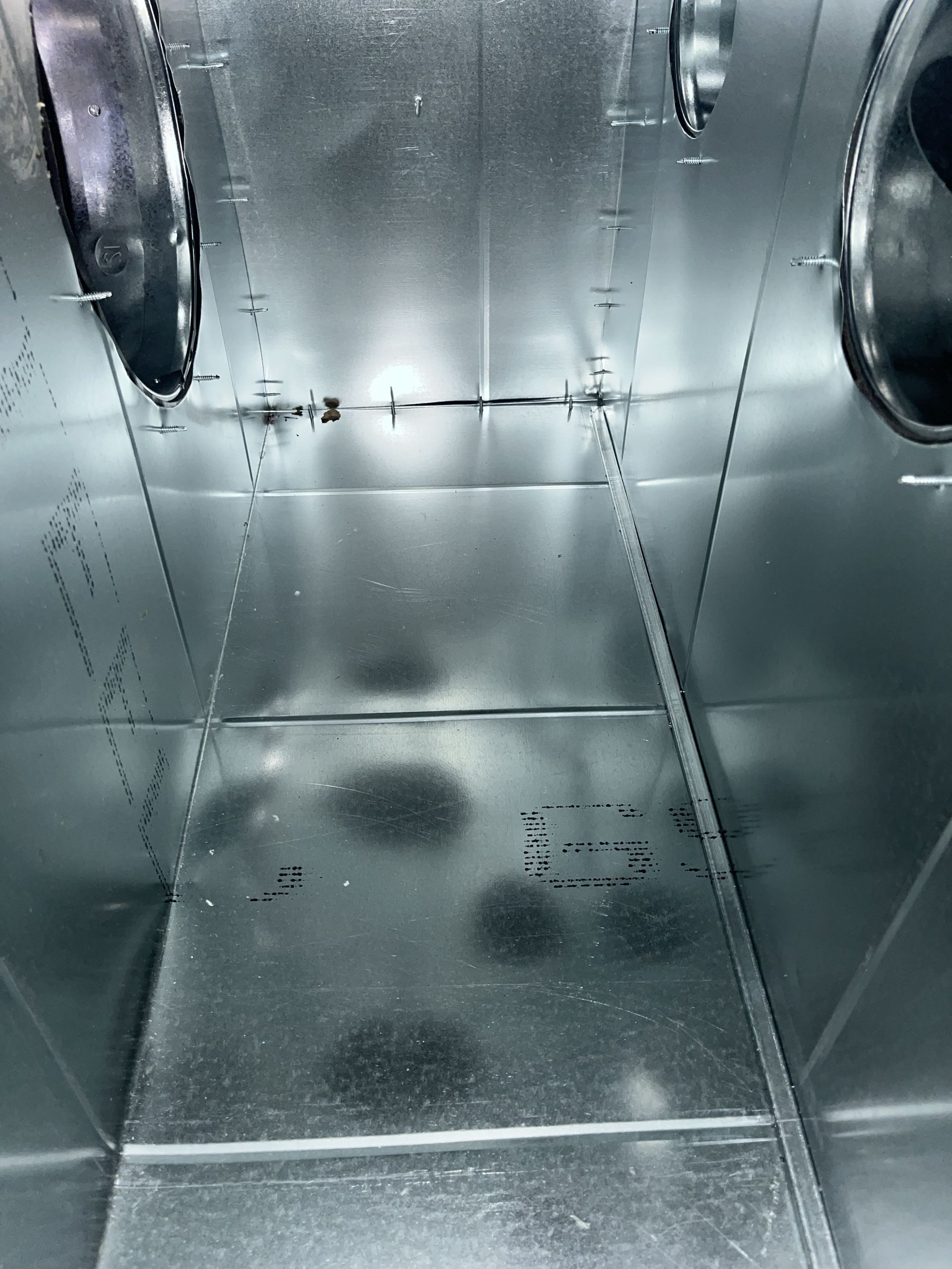 Shiny metal interior with riveted panels and circular openings, viewed down a narrow industrial duct.