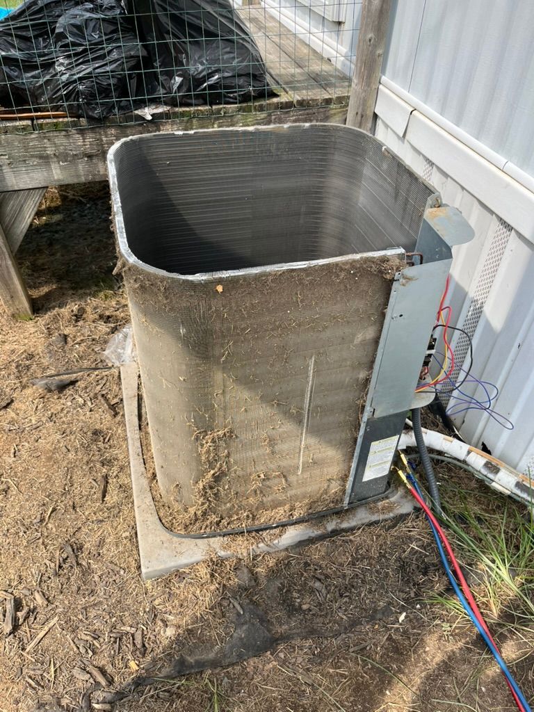 Dirty outdoor HVAC unit beside a building, with exposed wiring and gravel ground.