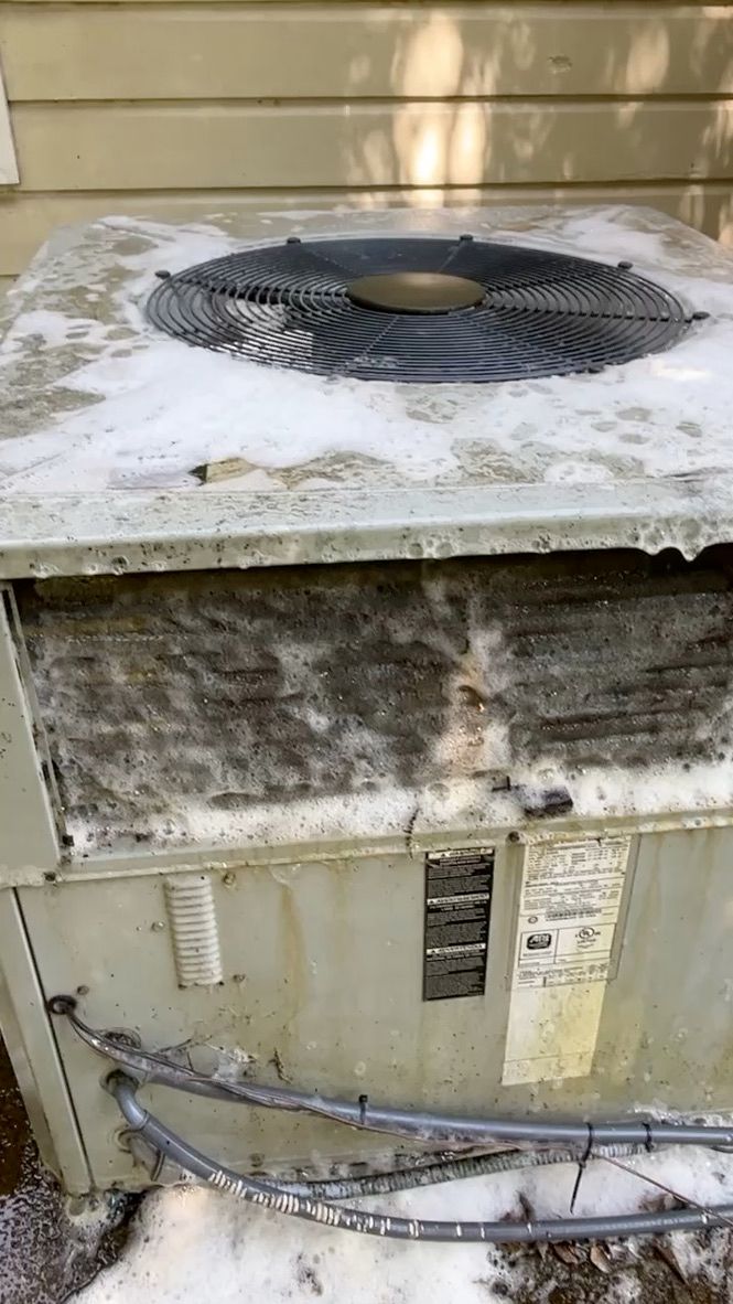 Outdoor HVAC unit with snow on top and dirty, weathered sides next to a beige house wall