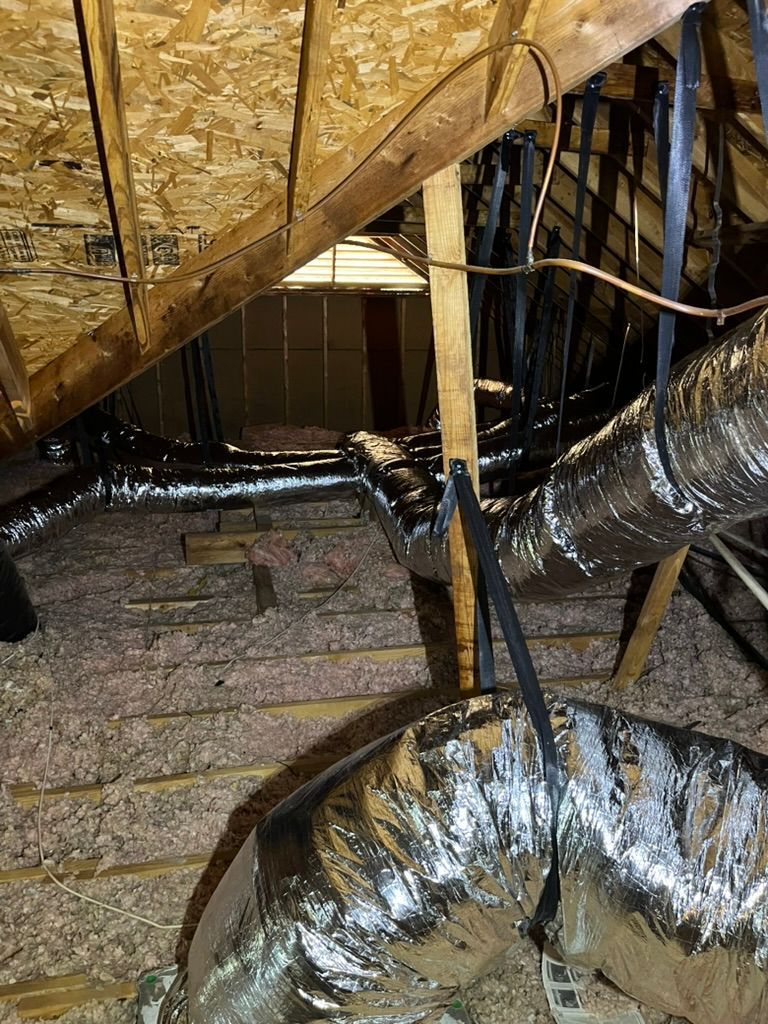 Insulated attic with exposed ductwork, wooden framing, and loose wiring under the roof