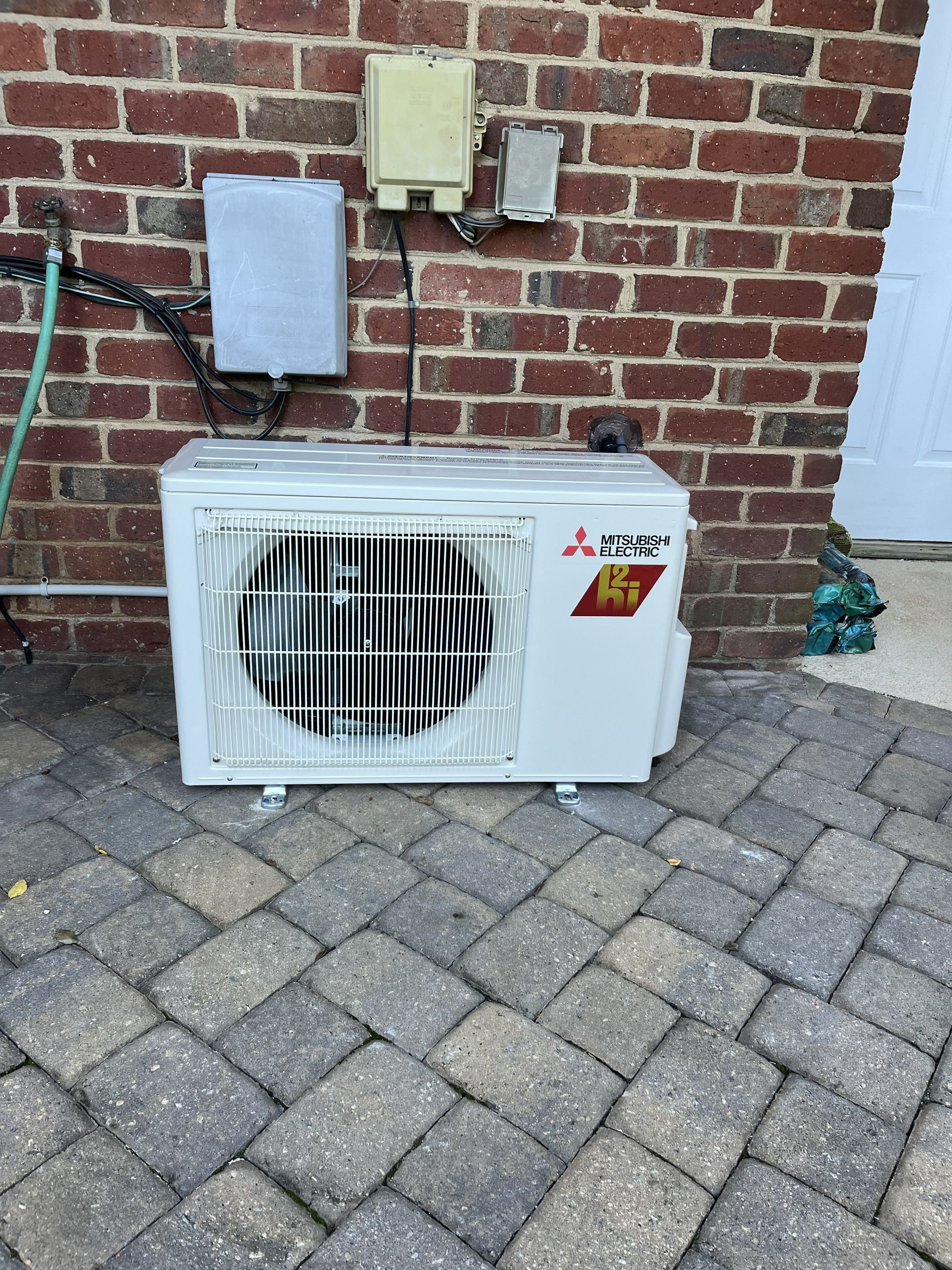 Outdoor Mitsubishi mini-split AC unit against a brick wall on a paver patio