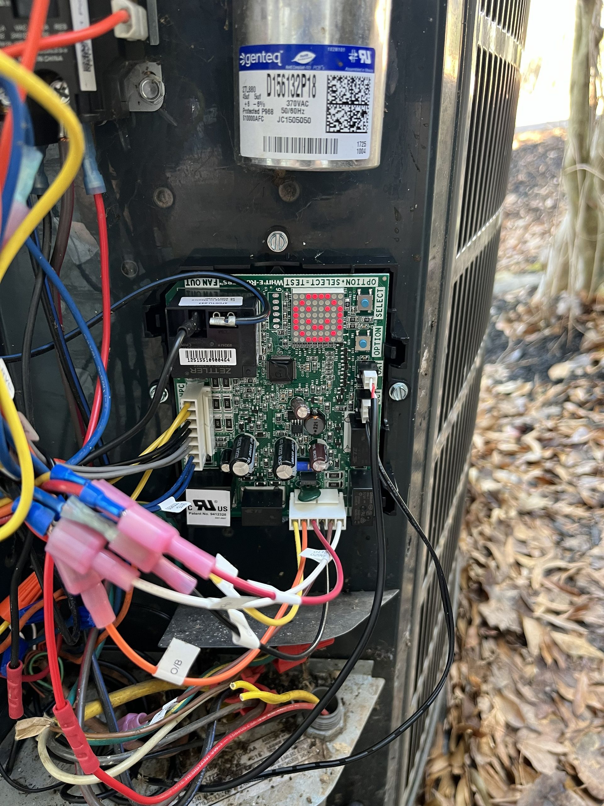 Close-up of an open electrical control box with wires and a circuit board inside, outdoors.