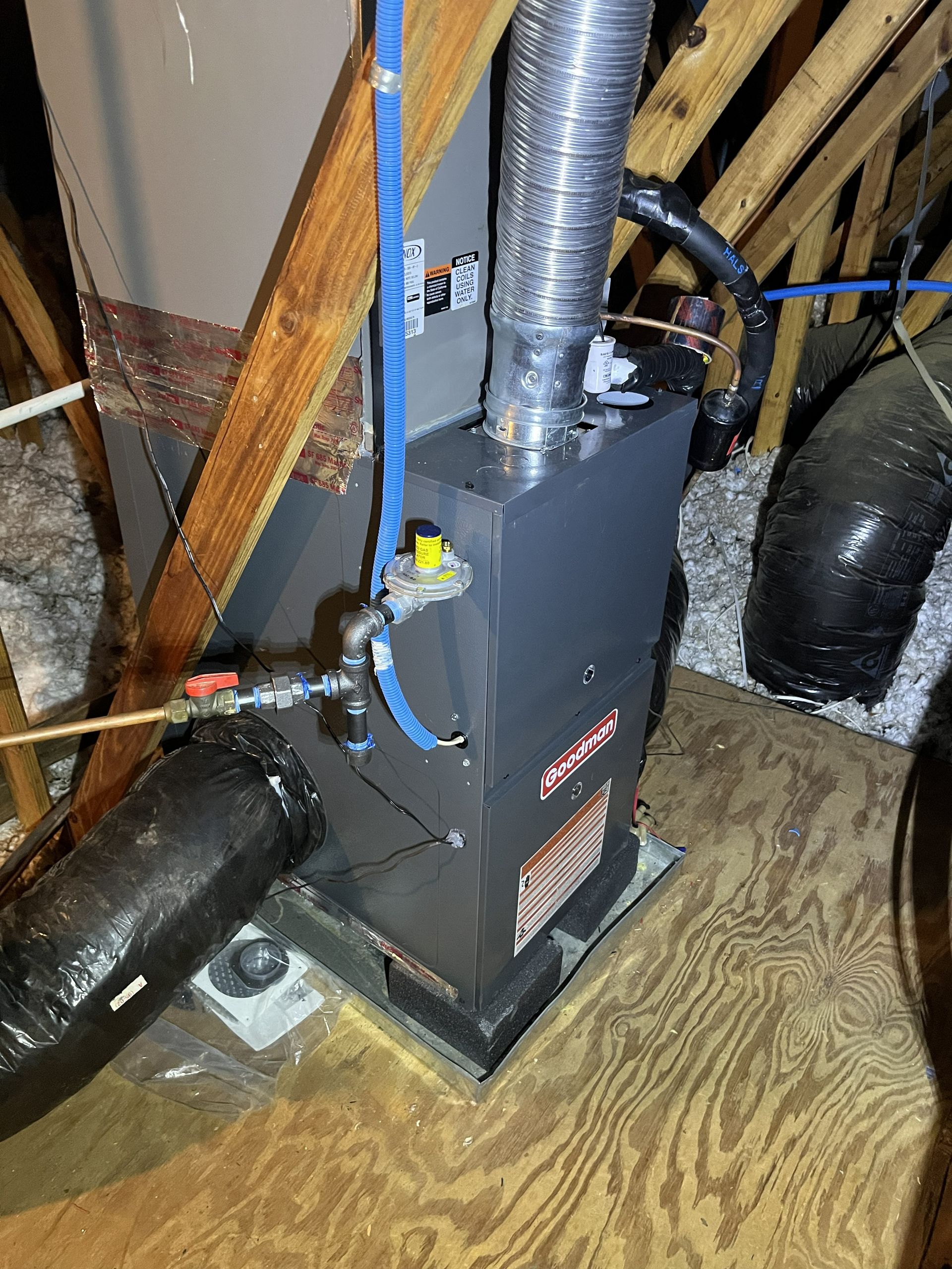 Gray HVAC furnace with silver ductwork in a basement on a plywood floor