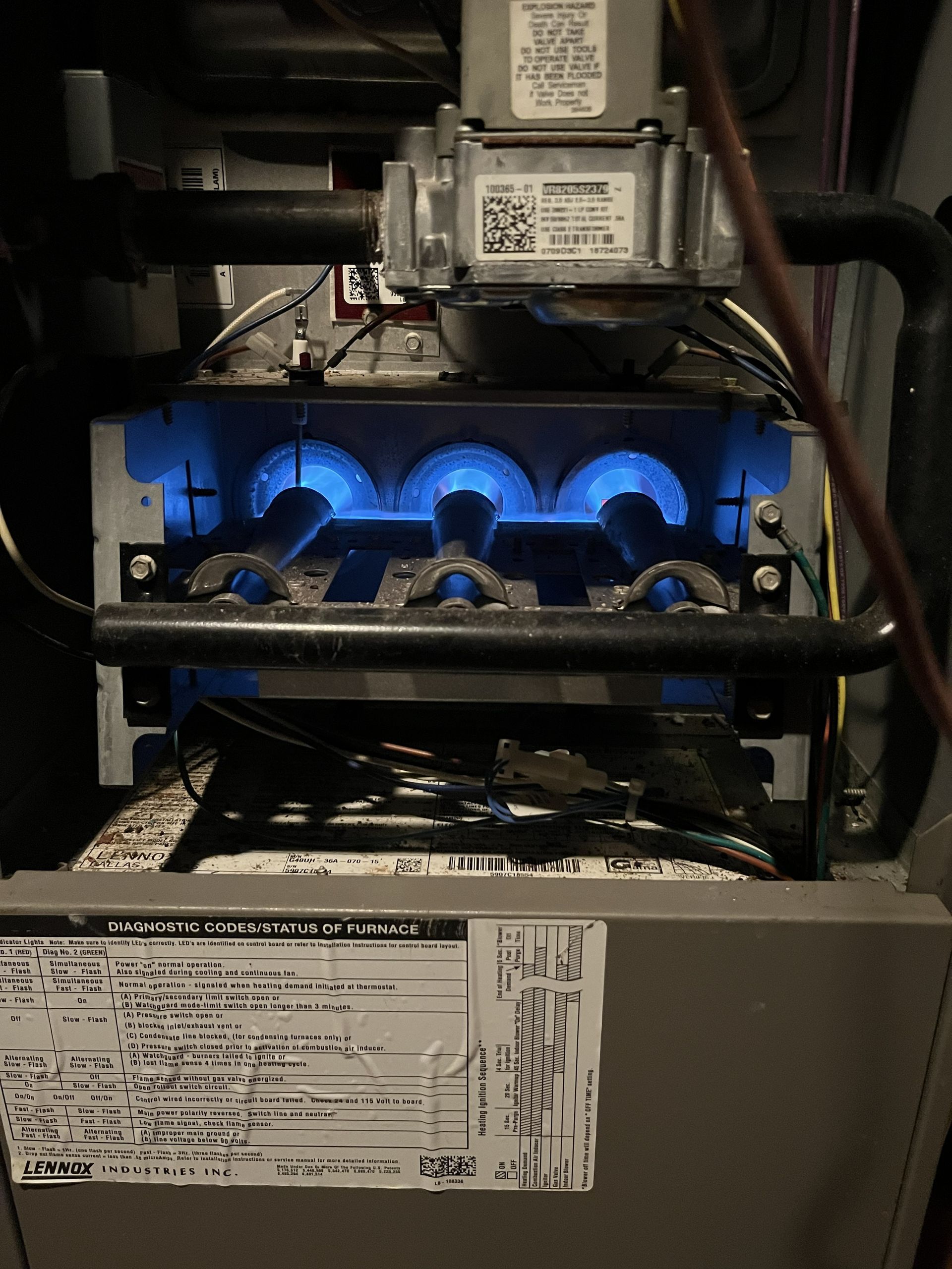 Blue-lit gas furnace interior with burners and control components visible behind an open panel