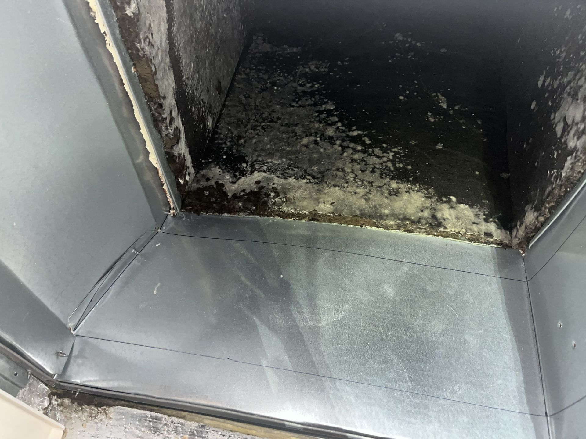 Charred, soot-covered interior of a metal vent or duct with burned residue at the top