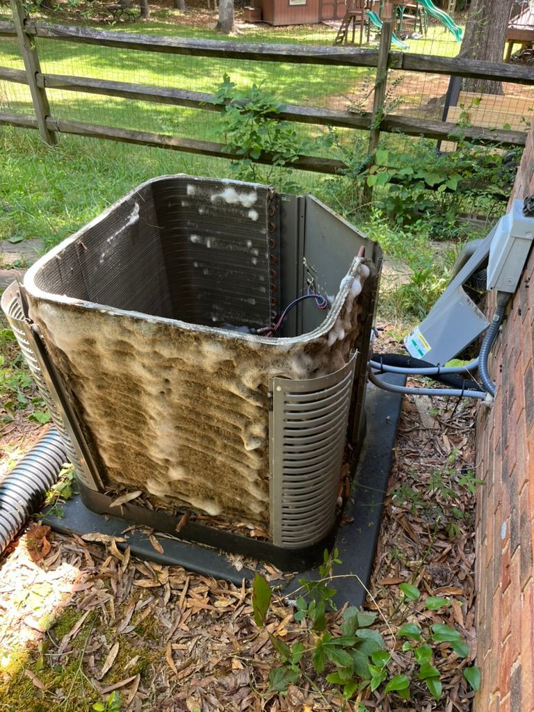 Old outdoor HVAC unit with rusted, dirty sides beside a brick wall and fence.