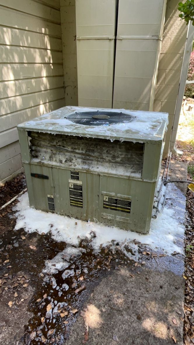 Outdoor HVAC unit covered with snow beside a house, with a snow-covered top and ground around it