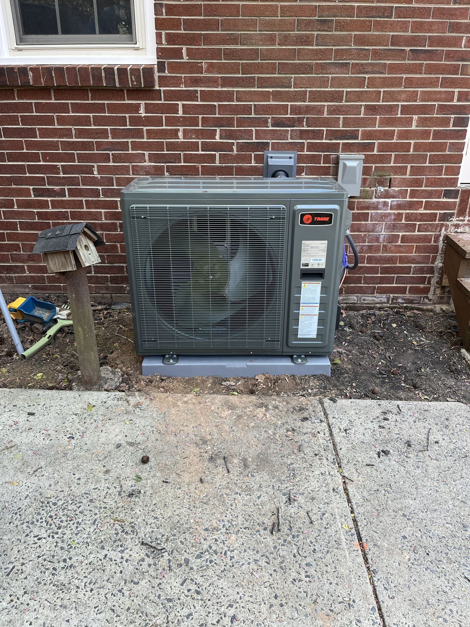 Outdoor HVAC unit beside a brick wall on a concrete pad with gravel around it