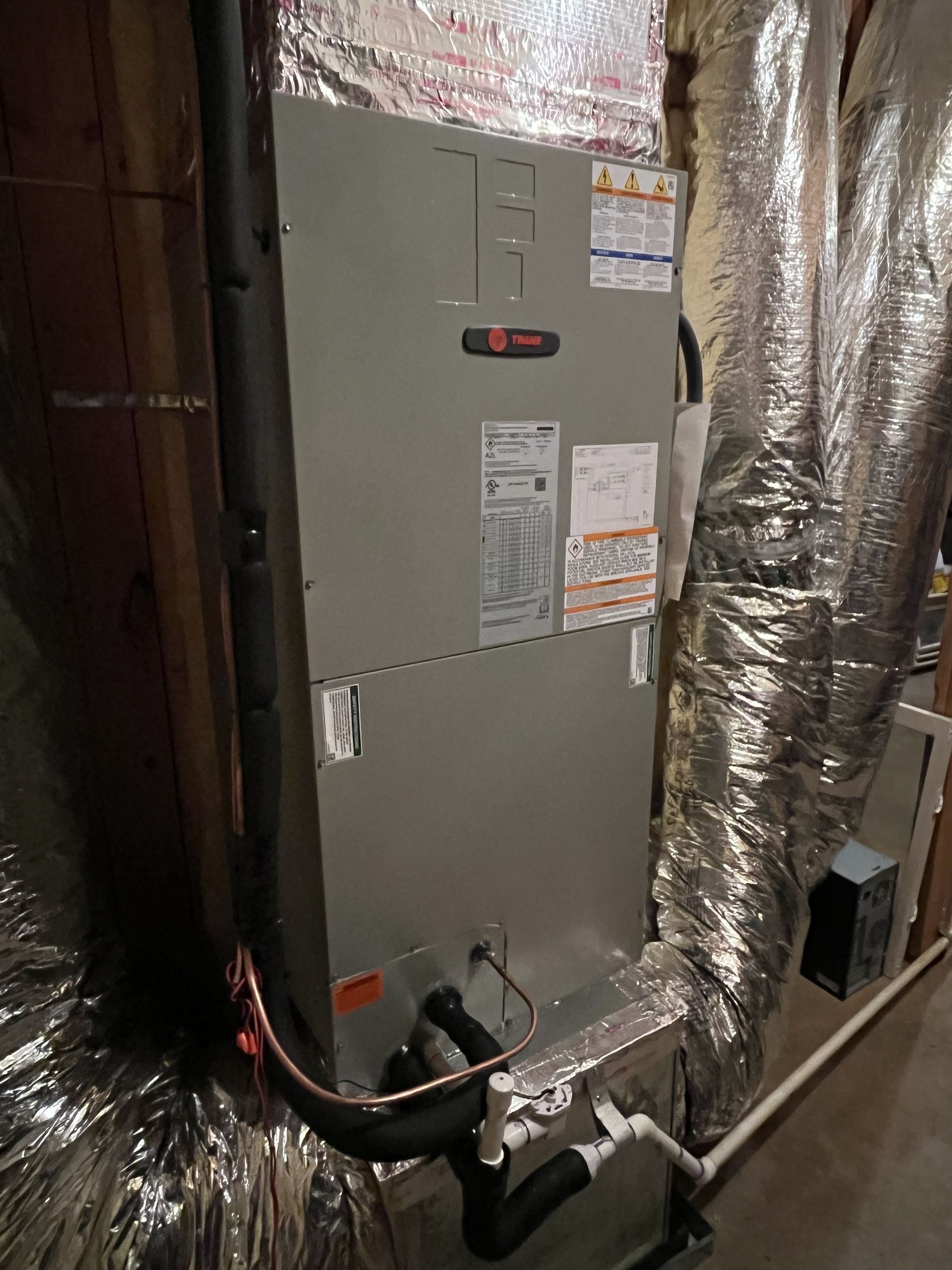 Gray HVAC furnace beside shiny insulated ductwork in a basement utility area